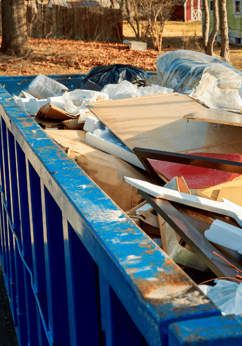 Large bin parked in front of a residential property, full of junk and debris.